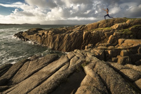 Distant Caucasian woman doing yoga on rocks near ocean