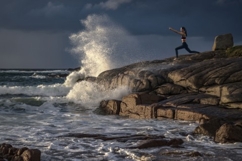Distant Caucasian woman doing yoga on rocks near ocean