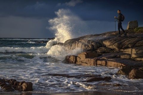 Distant Caucasian woman hiking on rocks near ocean