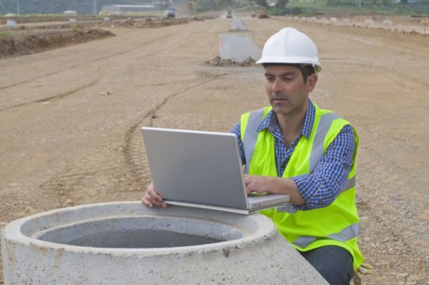 Hispanic construction worker using laptop in field