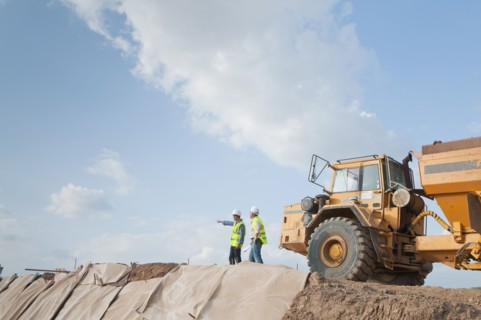 Hispanic construction workers in field with dump truck