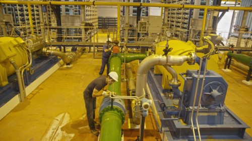 Hispanic workers examining pipes in factory