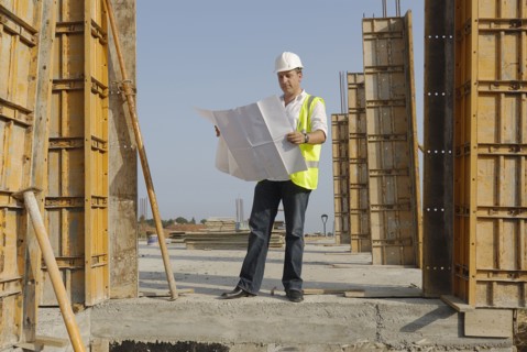 Male engineer wearing hard hat looking at plans on building site