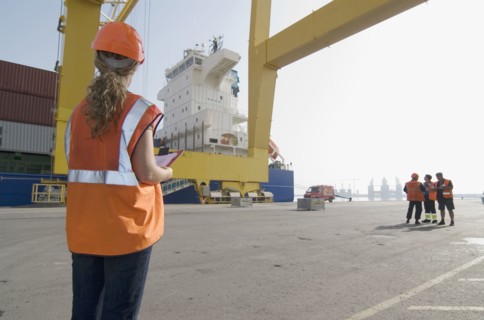 Woman wearing hard hat holding clipboard standing on dockside