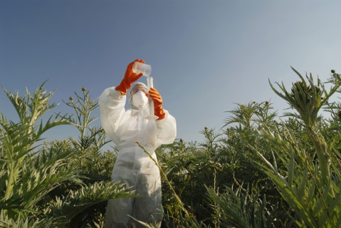 Woman in boiler suit standing in field pouring liquid into test tube