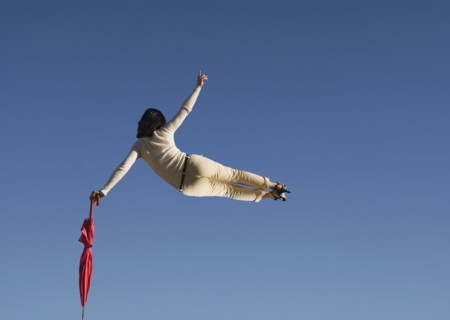 Woman in mid air clicking heels holding umbrella rear view