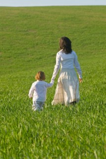 Mother and son holding hands in field rear view