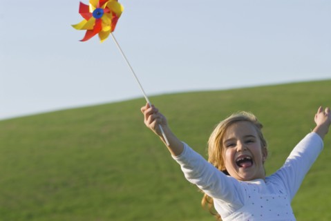 young girl with wind wheel running in green fields