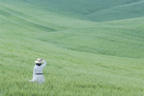 Woman in white dress walking through rolling hills of young wheat