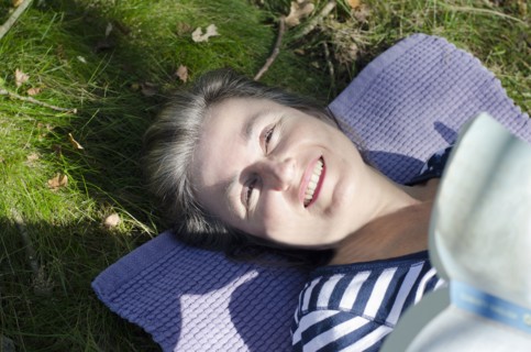 woman lying in grass on picnic rug holding book