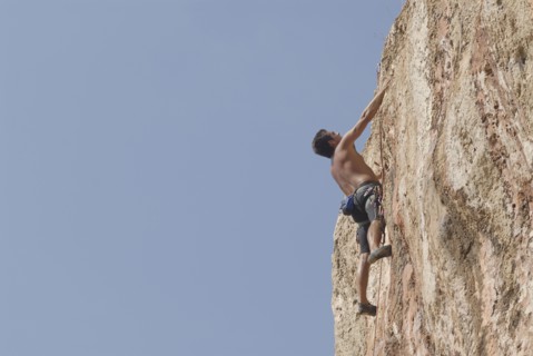 Male rock climber scaling rock face secured by ropes low angle view