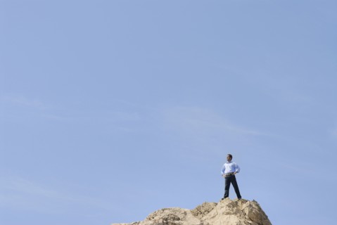 Businessman standing on top of rock looking into distance