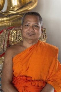 Thai Buddhist monk smiling near statue