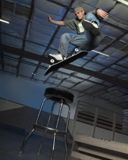 Caucasian man jumping on skateboard over stool indoors