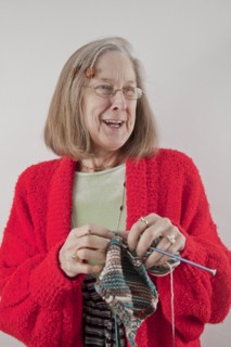 Caucasian woman wearing red sweater smiling and knitting