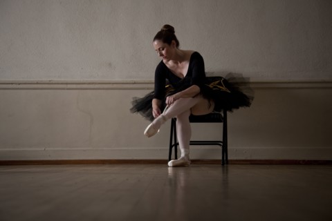 Caucasian ballerina sitting on chair tying ballet shoes