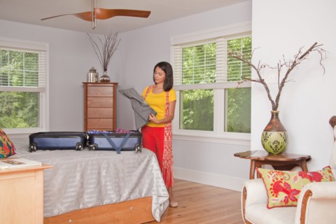 Hispanic woman packing suitcase in bedroom