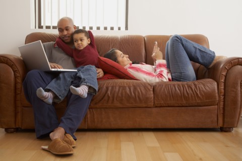 Antiguan man using laptop in living room with family