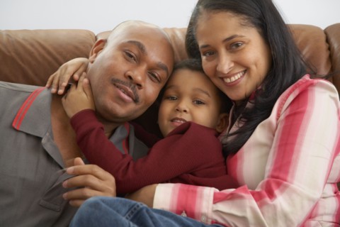 Mixed race boy snuggling on couch with parents