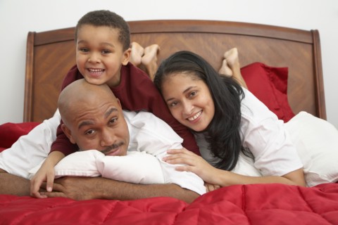 Mixed race boy lounging on bed with parents