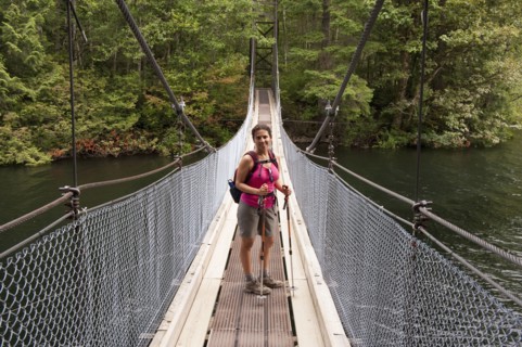 Hispanic woman hiking over bridge in woods