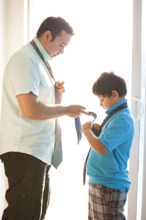 Hispanic father showing son how to tie necktie