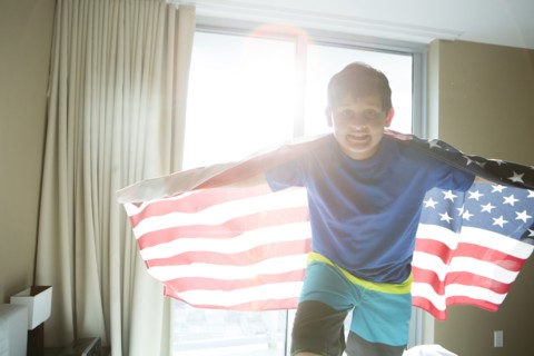 Hispanic boy using American flag as cape
