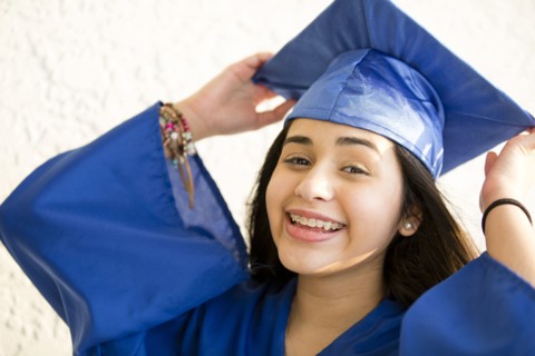 Smiling Hispanic girl wearing graduation robe and mortarboard