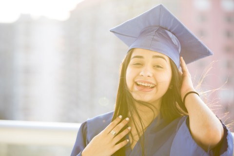 Smiling Hispanic girl wearing graduation robe and mortarboard