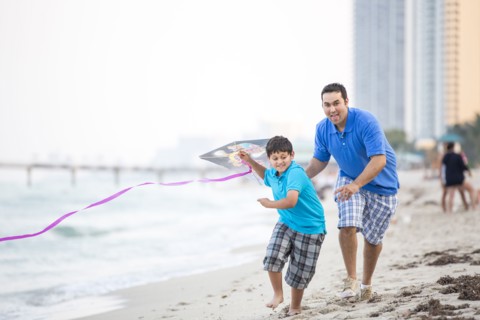 Hispanic father and son flying kite on beach