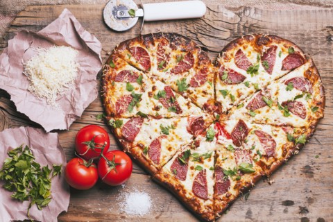 Heart-shaped pizza and ingredients on cutting board