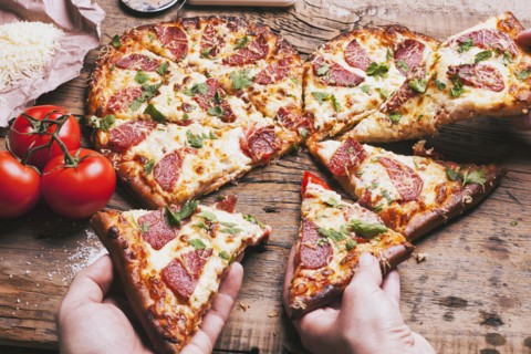 Hands pulling slices of heart-shaped pizza near ingredients on cutting board
