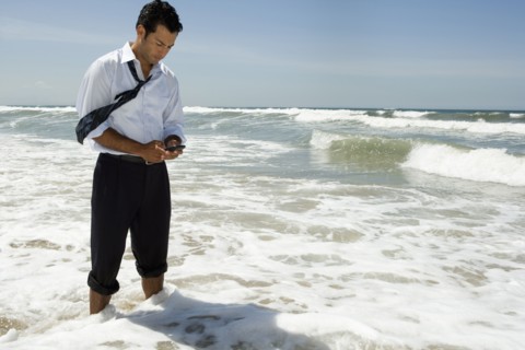 Businessman text messaging on cell phone while standing in ocean