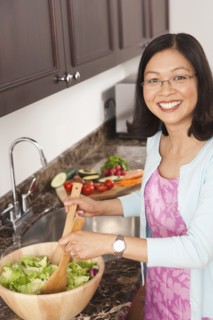 Chinese woman tossing salad in kitchen
