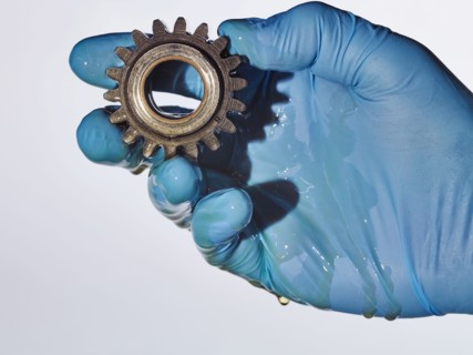 Hand wearing rubber-glove holding gear dripping with oil