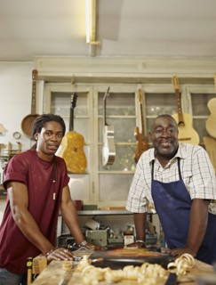Black craftsman in guitar workshop with son