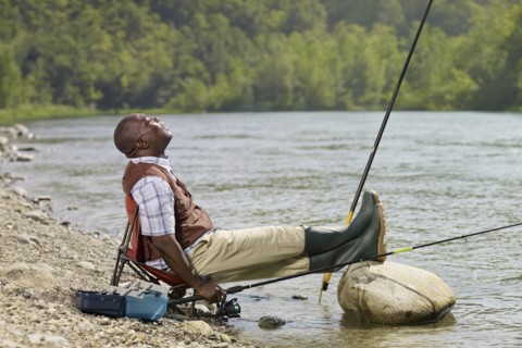 Black man with feet up fishing in stream