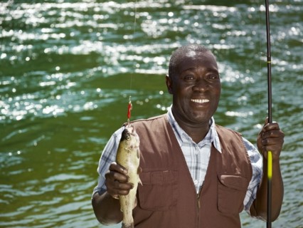 Black man holding fish and fishing rod near stream