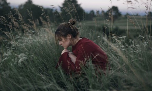 Pensive Caucasian woman sitting in tall grass