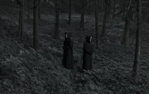 People wearing black robes and white masks in forest