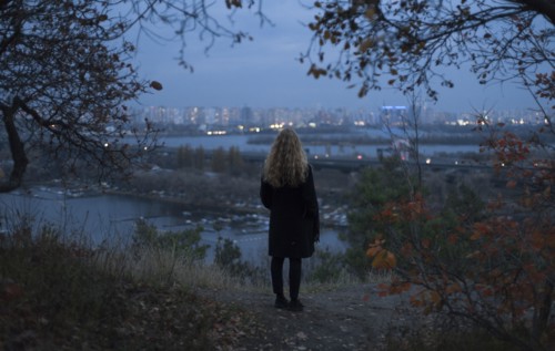 Pensive Caucasian woman standing near urban waterfront at night