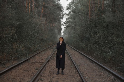 Caucasian woman holding autumn leaf on train tracks in forest