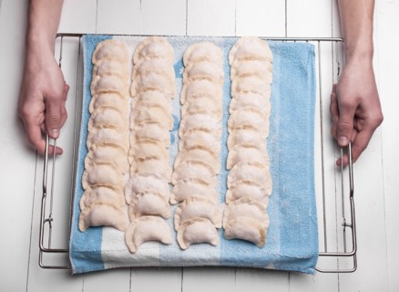 Hands holding rows of pierogies on towel