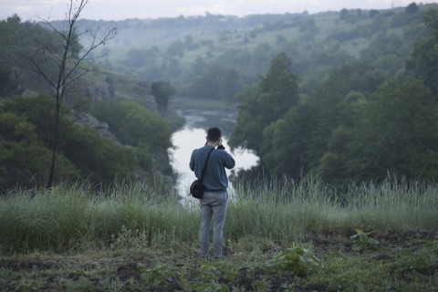 Caucasian man standing on hill photographing river
