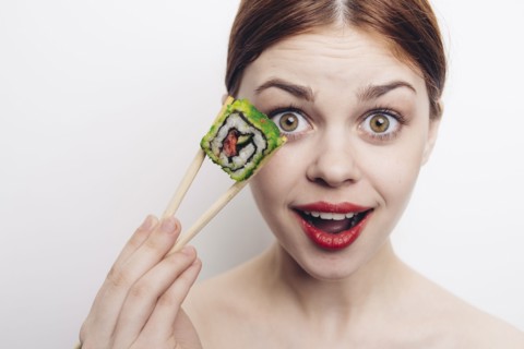 Caucasian woman holding sushi with chopsticks