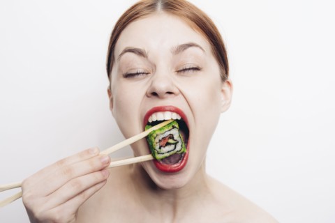 Caucasian woman eating sushi with chopsticks