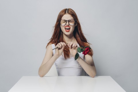 Caucasian woman sitting at windy table snapping stem of rose