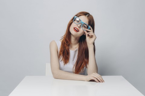 Pensive Caucasian woman sitting at table wearing blue eyeglasses