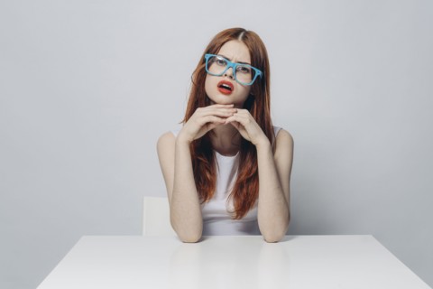 Angry Caucasian woman sitting at table wearing blue eyeglasses