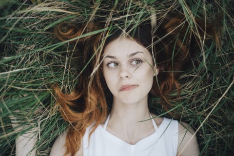 Caucasian woman laying in grass blowing hair off face
